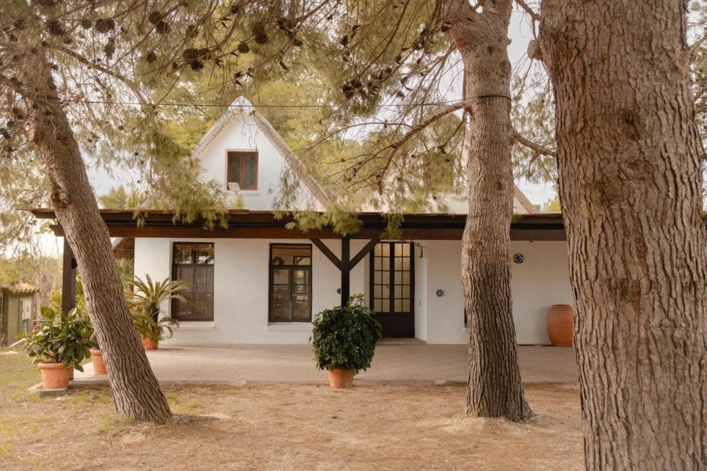Entrada principal de una barraca valenciana rodeada de pinos en Jardin Les Barraques, Albufera de Valencia